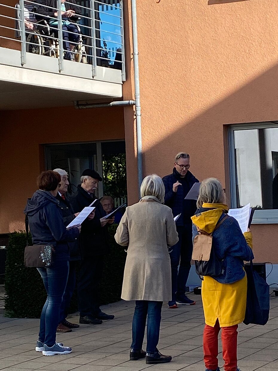 Chorleiter und einige Chorsänger und -sängerinnen im Innenhof des Wohnheims